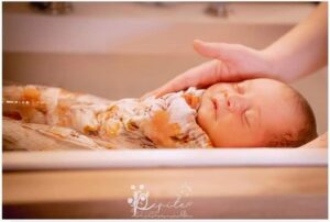 Thalasso bain de bébé : un nouveau-né endormi dans un bain et emmailloté dans un lange en coton fleuri